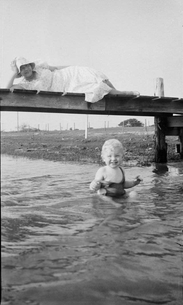 Child sitting in water with a woman laying on a walkway above him