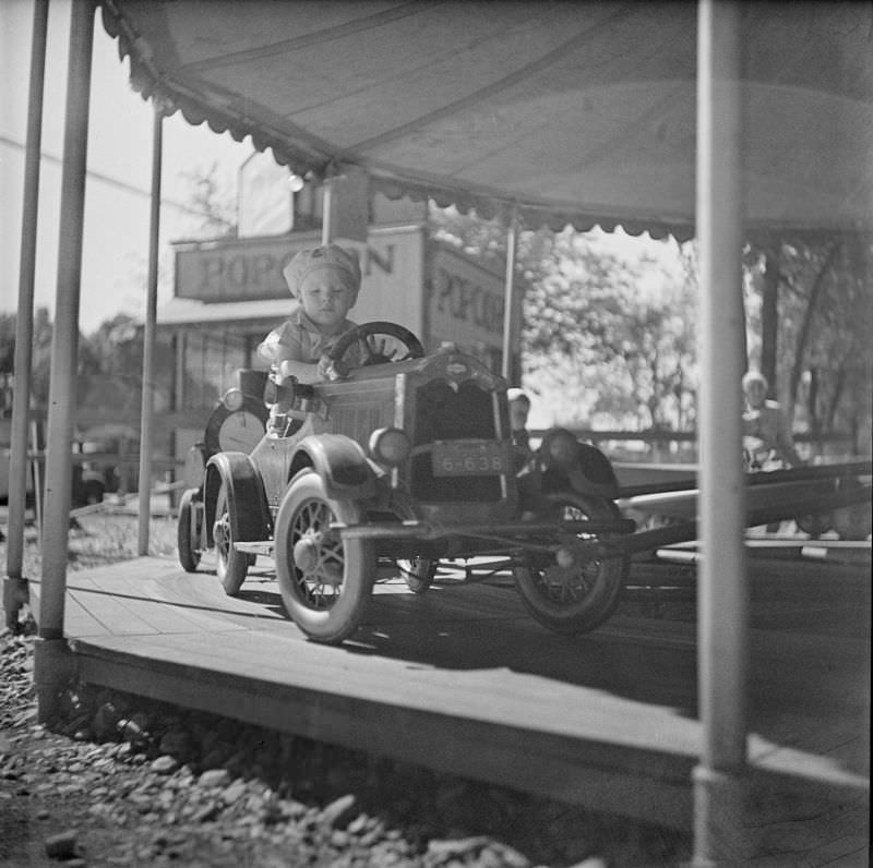 Little boy sitting in toy car on carousel at amusement park