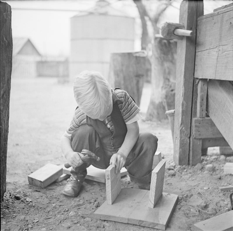 Boy holding a small hammer, kneeling next to a couple wood planks