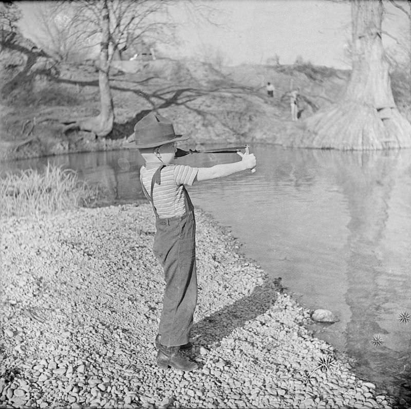 Boy playing with a toy slingshot, standing on a river bank