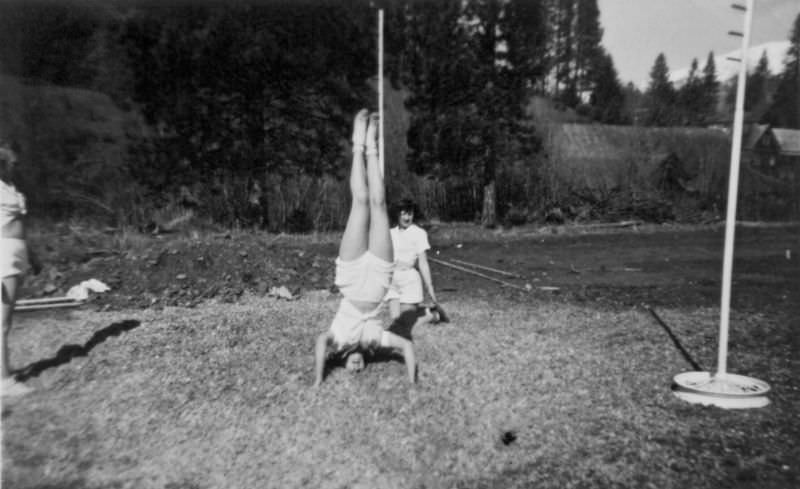 A teenage girl performs a headstand while a couple other watch