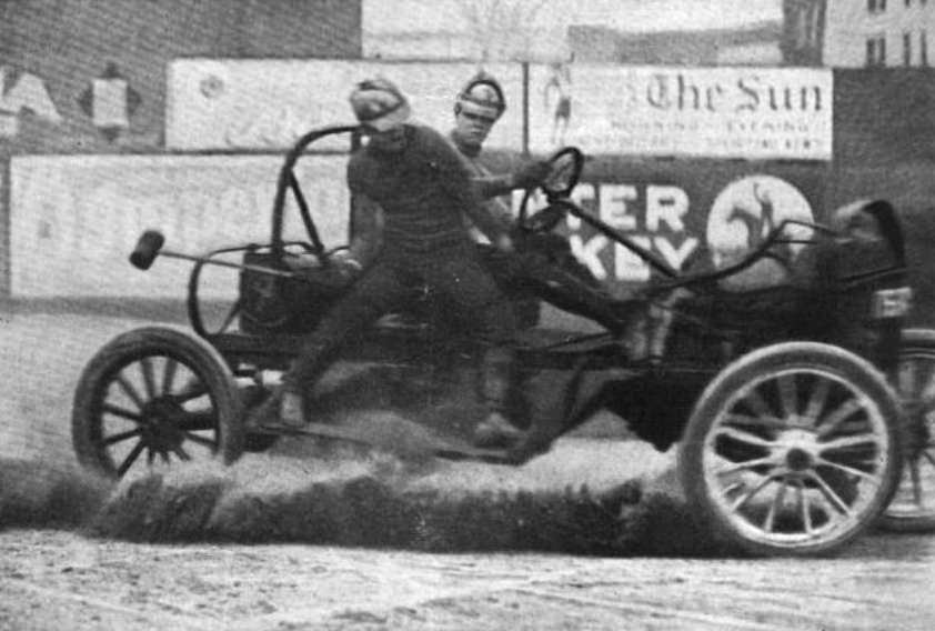 A malletman balances on the side of a moving auto polo car during a match at Hilltop Park, New York