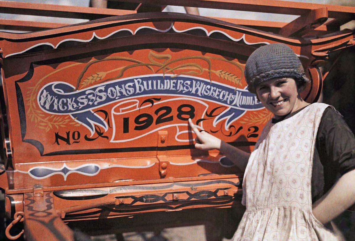 An English woman points pridefully to her farm cart, in Cambridgeshire, England. Wicks of Wisbech constructed horse-drawn caravans used by Romany families traveling throughout Britain.