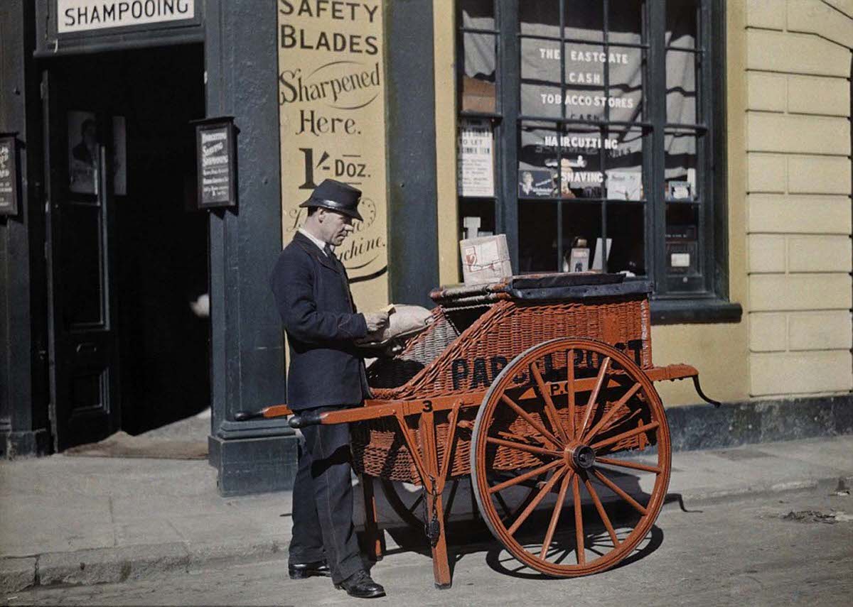 A postman delivers packages with his parcel post barrow in front of a shop in Oxford offering ‘haircutting and shaving’ in 1928.