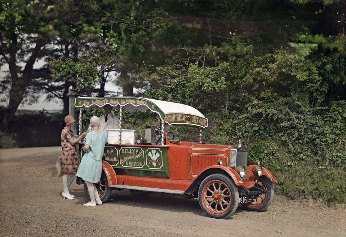 Two women buy ice cream from a vendor out of his converted car, in Cornwall. Kelly’s ice cream is still in production today.