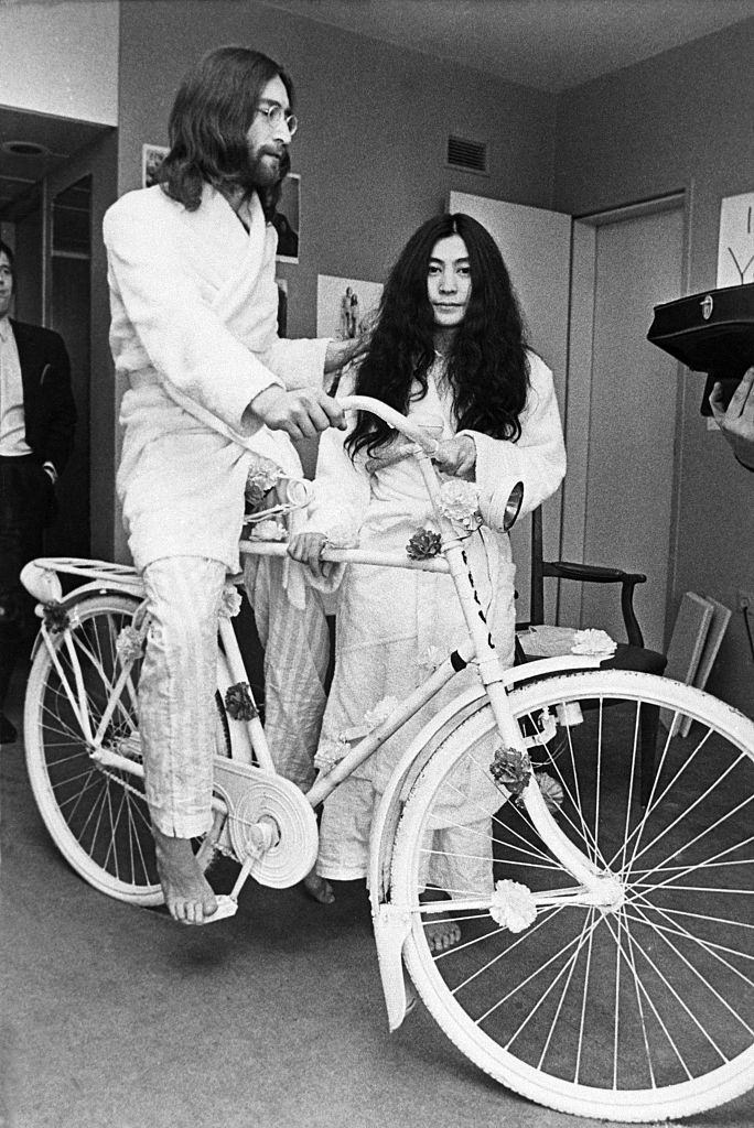 Beatle John Lennon tries out a bicycle he received as a gift while his new wife, Yoko Ono, stands by in Amsterdam, 1969.