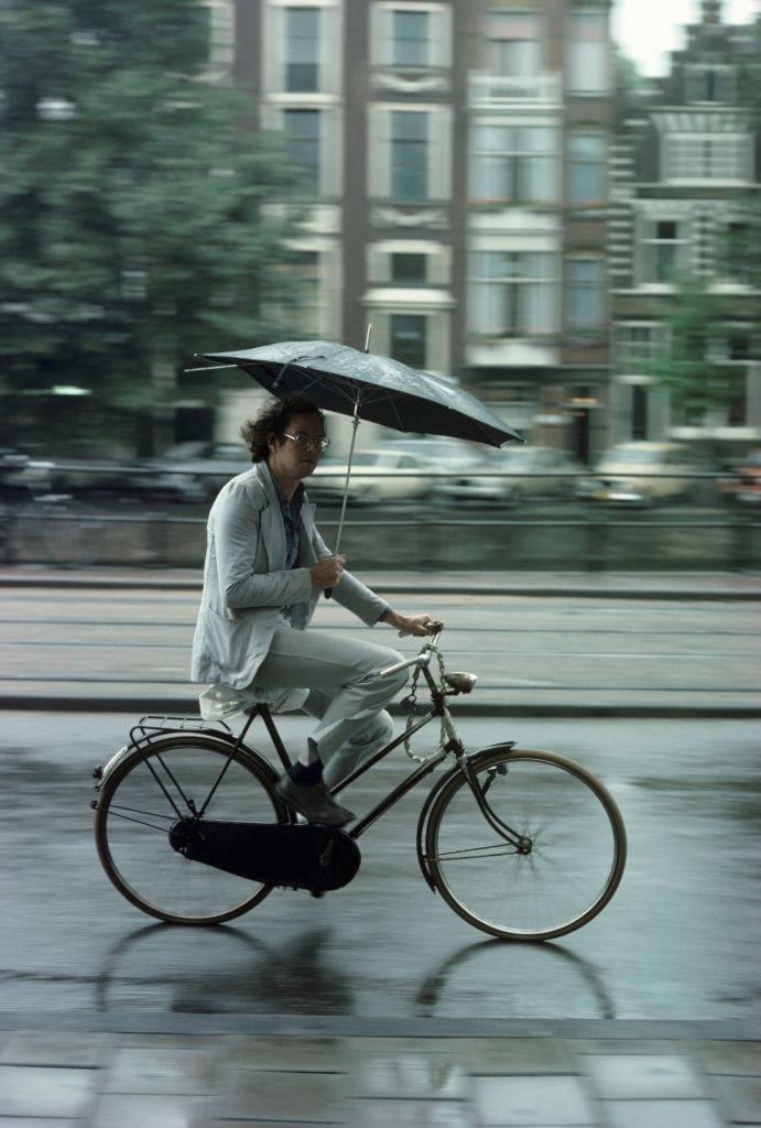 A cyclist holding an umbrella riding through the rain in Amsterdam, 1976.