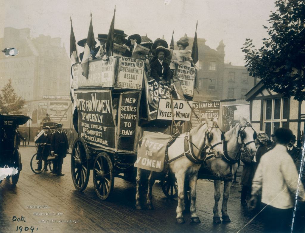 A group of suffragettes on board a cart advertising the newspaper Votes for Women, containing articles by Emmeline Pankhurst.