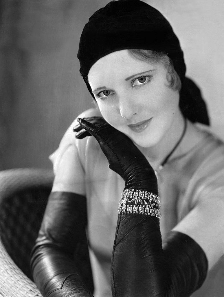 Jean Arthur with hat and long, black leather gloves and arm jewelry, 1930.