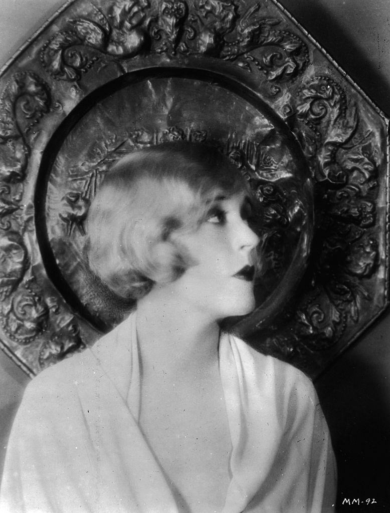 Mae Murray poses in front of an ornamental plaque, 1925.