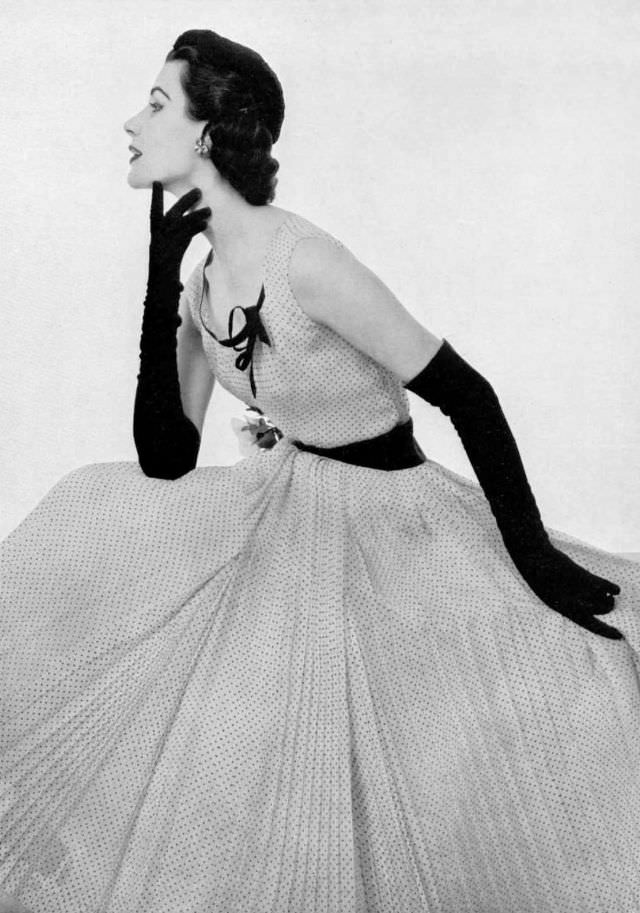 Myrtle Crawford in finely pleated, white muslin dress dotted in black, sleeveless bodice is decorated with black ribbon, black gros-grain belt holds pink rose, by Madeleine de Rauch, 1953