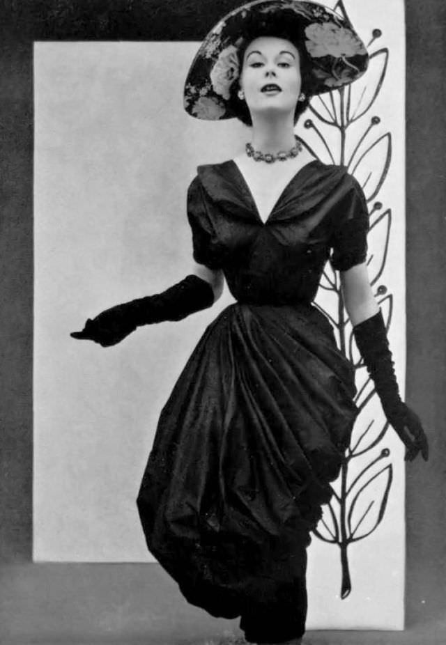 Myrtle Crawford in draped taffeta dress that is rolled up in a style reminiscent of that of a washerwomen's apron, by Grès, hat by Gilbert Orcel, 1952