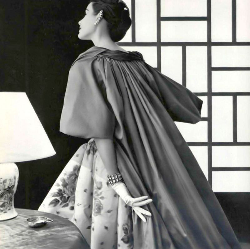 Myrtle Crawford in Venetian style cloak of coral taffeta, worn over white and pink floral print taffeta dress by Jean Patou, 1954.