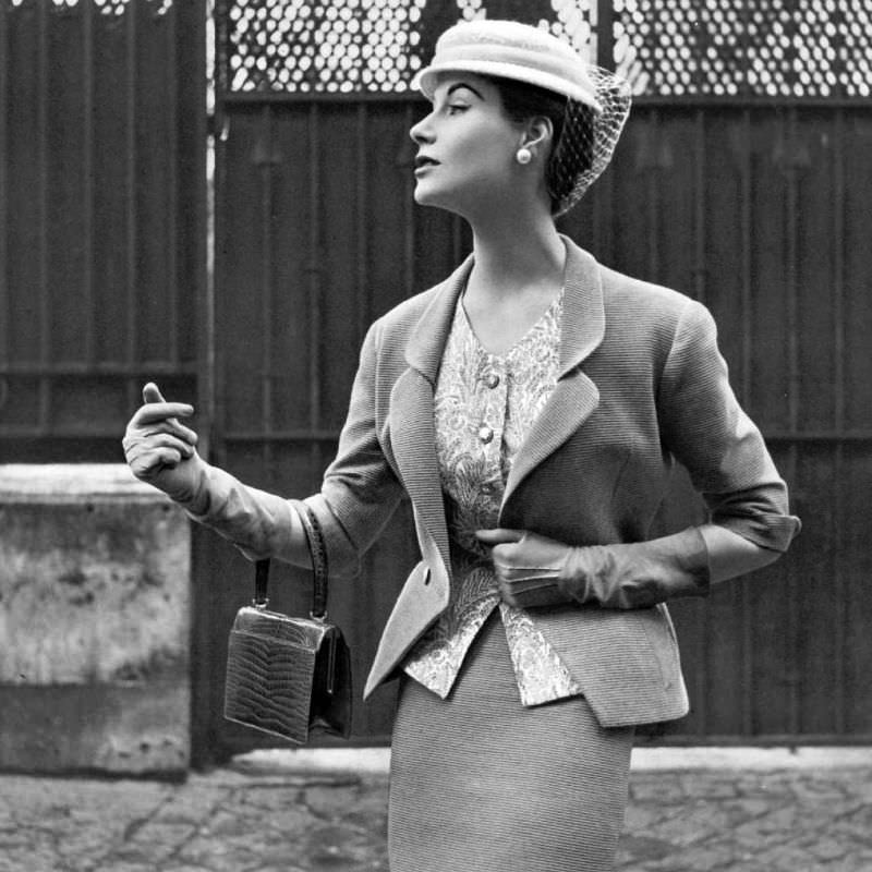Myrtle Crawford in beige Ottoman suit with fitted jacket indented to v, worn over print cashmere top and narrow skirt by Manguin, hat by Paulette, croc bag by Morabito, 1953