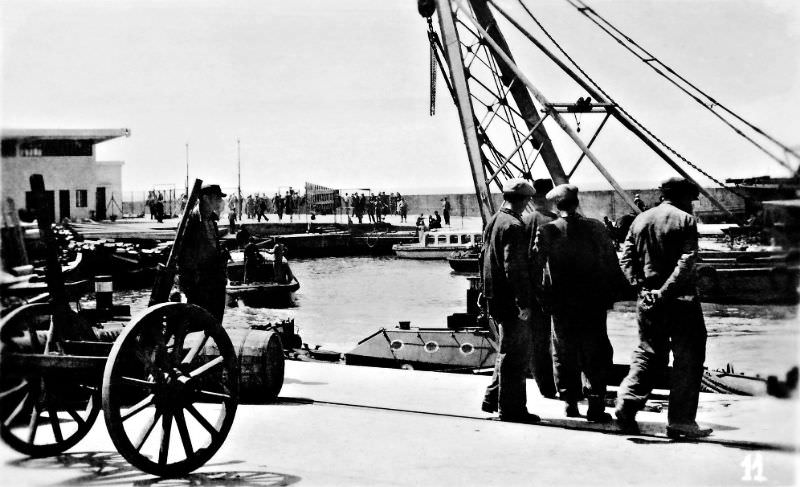 Looking south-west across the old Tel Aviv port facility as dock workers wait next to a port crane, Tel Aviv, Palestine (now Israel), 1937