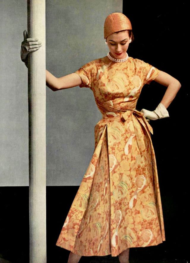 Anne Gunning in silk print dress of various shades of yellow with pleated panels in the skirt and a crossed bodice by Givenchy, 1953