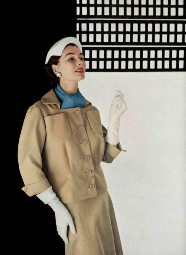 Anne Gunning in tan cotton piqué suit, jacket is boxy with square neckline, bright blue scarf adds color, by Jean Patou, 1953