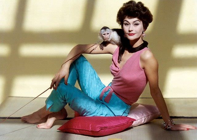 Anne Gunning in cashmere wrap top and silk capri pants poses with Capuchin monkey on her shoulder, 1958.