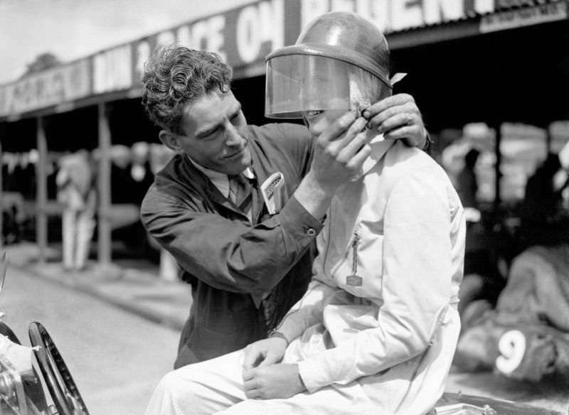 A Brooklands’ mechanic fastens the buckle on Miss Dorothy Turner’s helmet, July 1937.