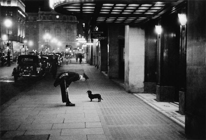 A hotel commissionaire talking to a small dachshund dog in piccadilly circus, London, 1938