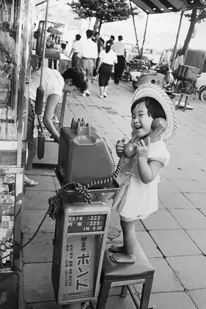 A little girl having fun pretending to talk on the telephone, Japan, 1958