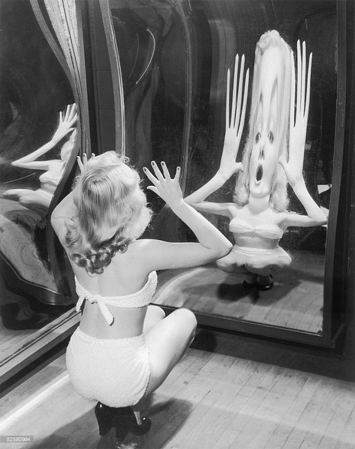 A woman in a toweling bikini poses in a funfair hall of mirrors, 1935