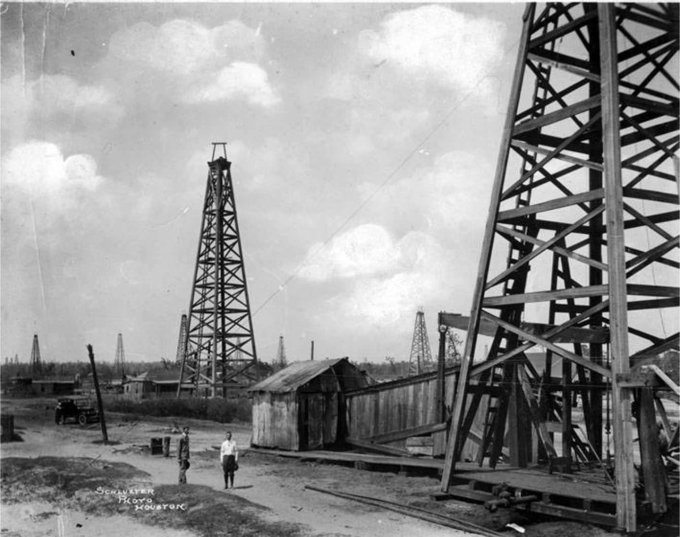 Two men standing on dirt road near an oil well, 1930s.