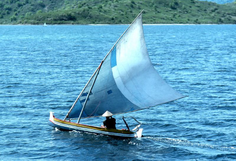 Balinese fisherman in traditional sailing vessel drags a line off the coast of Bali, 1970s