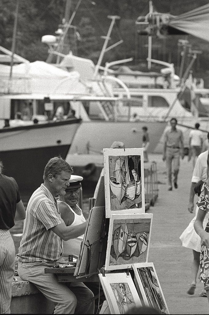 A man painting on the dock of a harbor, Italy, 1960s.