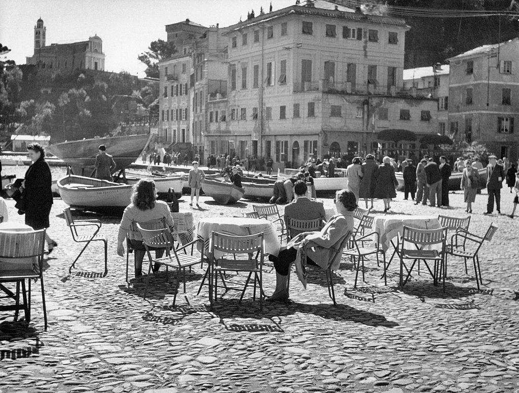 People sitting at the small outdoor tables of a bar in Portofino, 1960s.