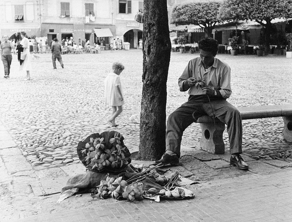 A young man sitting on a bench creates bunches of papier-maché flowers, Portofino, 1960s.
