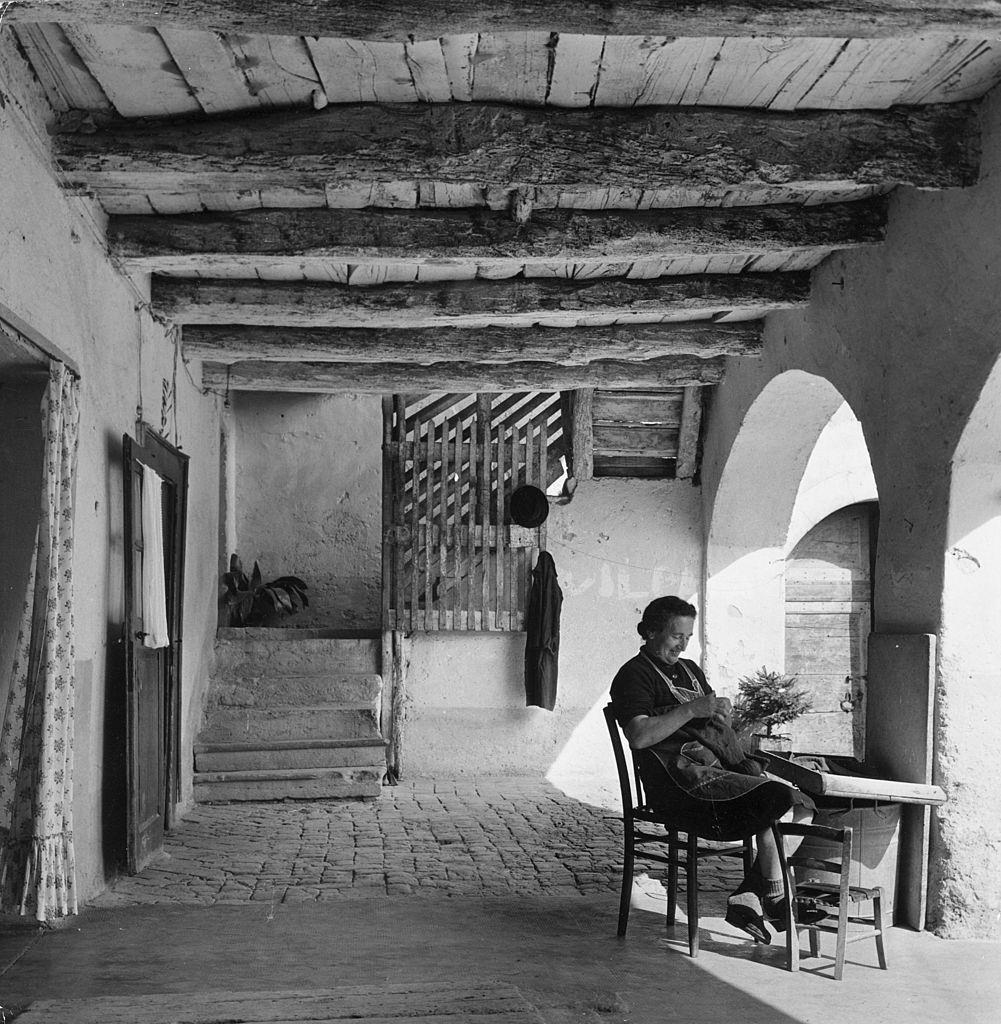 Signora Allessandra Roncalli sits knitting in a covered courtyard, 1960s.
