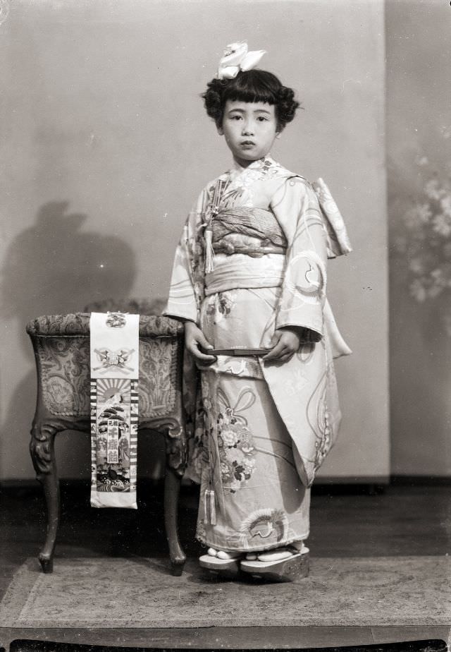 A Japanese girl in a kimono with a bow, geta sandals, and folded fan. She also has the traditional Shichi-Go-San Chitose Ame candy