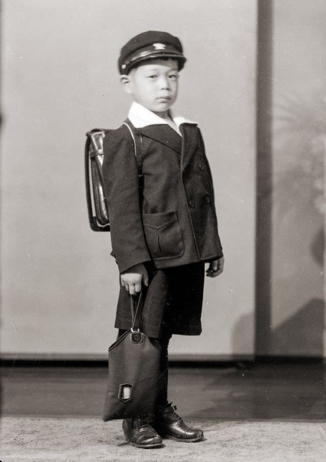 A Japanese school boy in a uniform, hat, and backpack