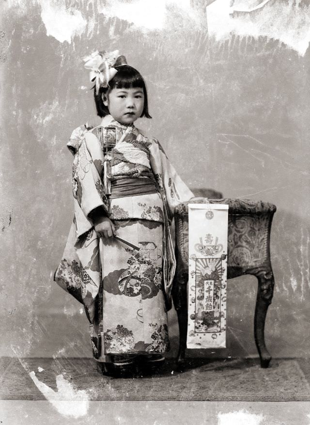 A young Japanese girl in a kimono and hair bow and holding a bow as well as traditional Shichi-Go-San candy