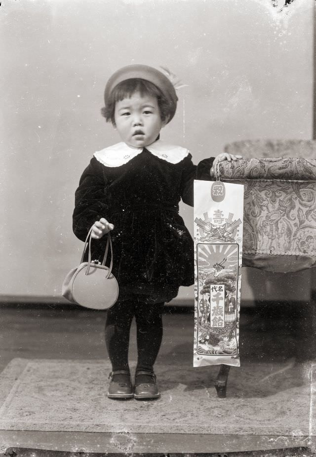 A young Japanese girl in a velvet blouse and hat and holding traditional Chitose Ame candy for Shichi-Go-San