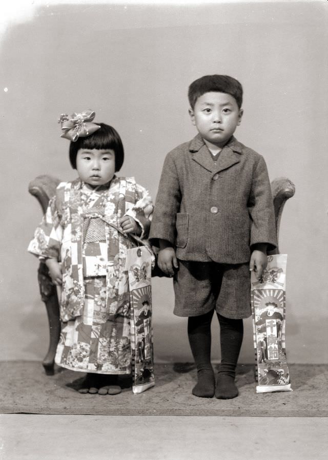A young Japanese girl in kimono and a young boy in a shorts suit - both of them holding Chitose Ame candy for the Shichi-Go-San Festival