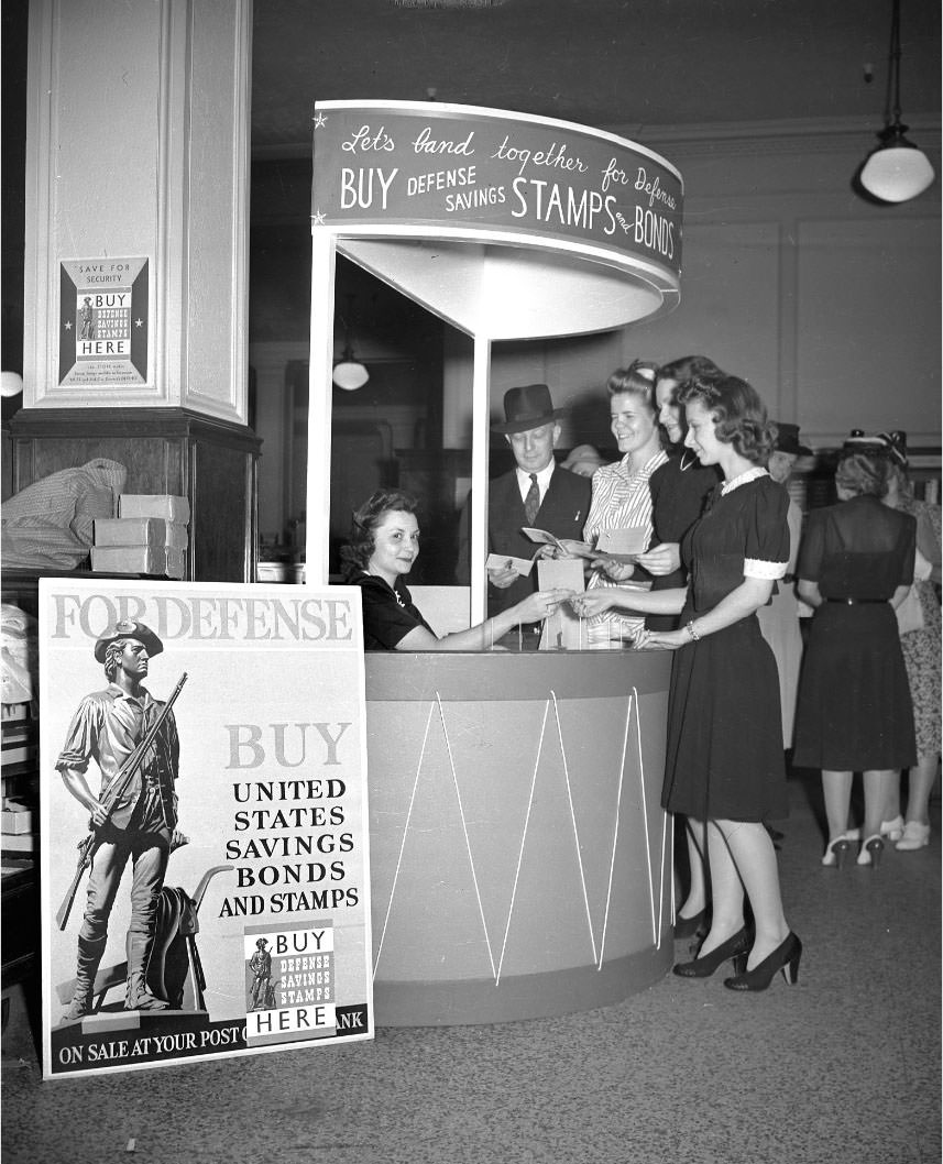 A woman seated at a kiosk inside an unidentified building in Nashville, selling Defense Savings Stamps and Bonds.