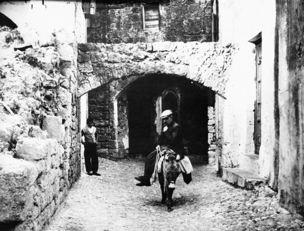 Man riding a donkey in the streets of Rhodes, 1910s.