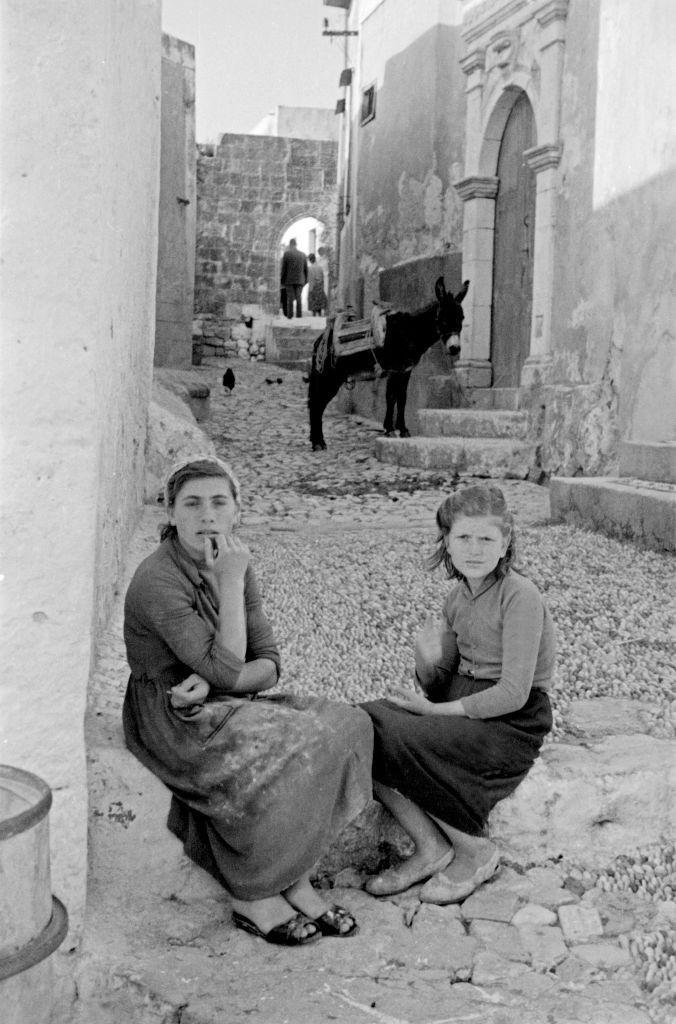 Two young women sit in front of the house on the street having a conversation in Rhodes, Greece, 1950s.