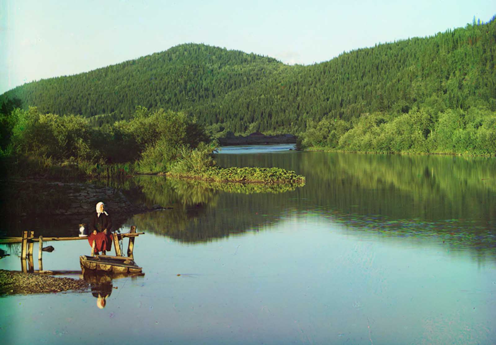 A woman is seated in a calm spot on the Sim River, part of the Volga watershed in 1910.