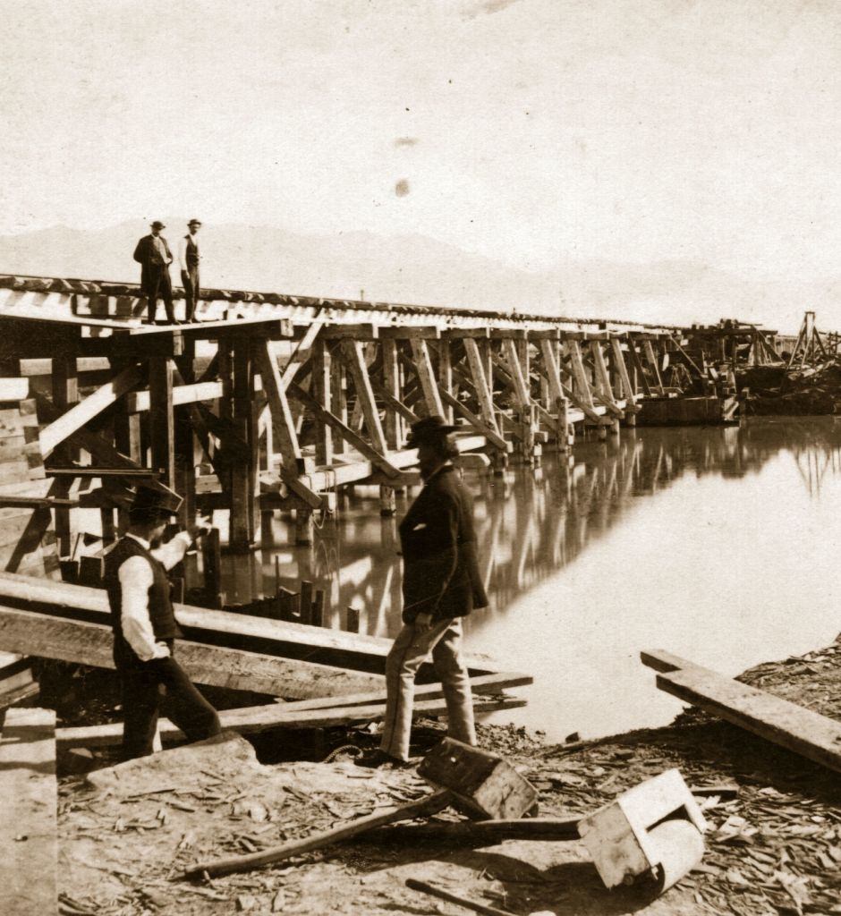 The building of the railway bridge over the river at Salt Lake City in Utah with the beginnings of a settlement by the Mormon sect evident.