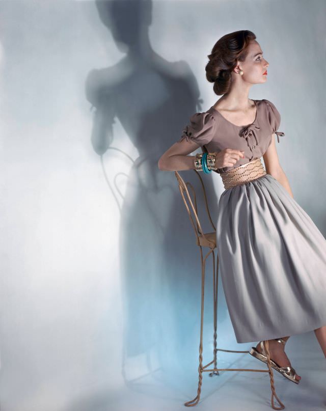 Model in cocoa, short-sleeved blouse and beige skirt, wide leather belt with gold buttons by Criterion, gold sandals, 1946