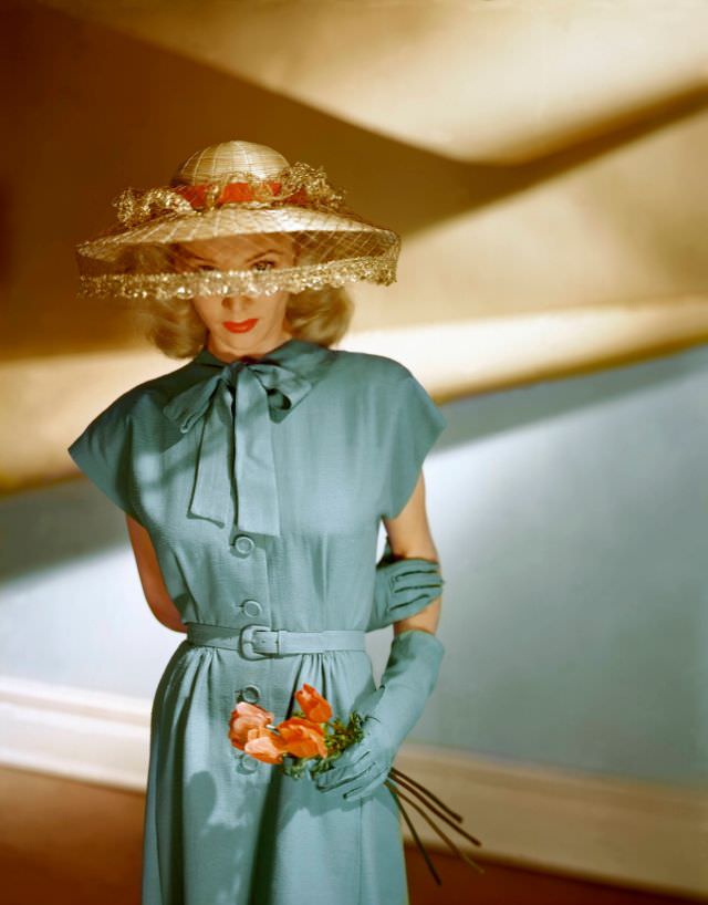 Actress Carole Landis wears a short-sleeved blue dress from a Vogue Pattern together with matching gloves and John Frederics veiled hat, 1945