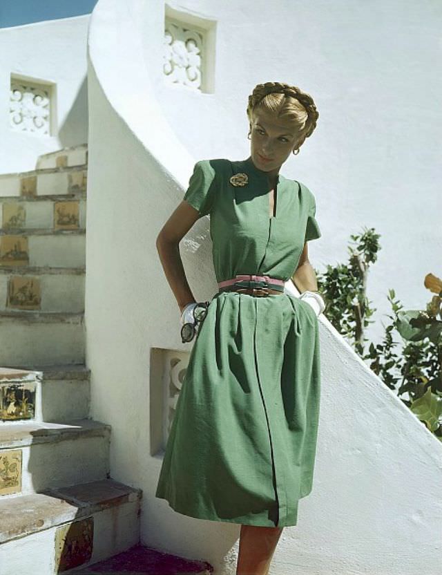 Bijou Barrington in grass-green shantung dress with slot neckline, unpressed pleats, Coro pin, Vogue belts, Glamour, 1945