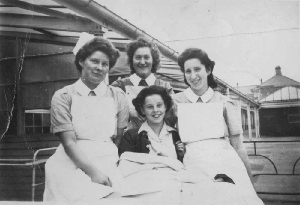 A young patient resting in bed outside, accompanied by three nurses at Stannington Sanatorium, 1946.