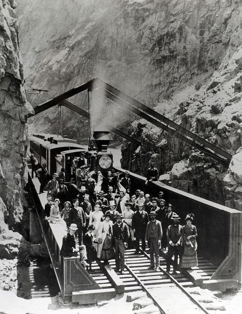 Passengers and crew of the Denver and Rio Grande Western Railway stand by the train as it stops by a cutting cut through the mountains, 1885.