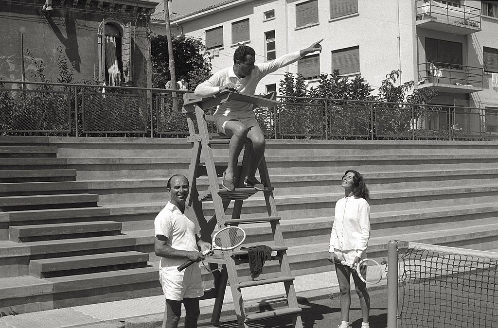 The actor Alberto Sordi makes a pretence of being umpire, sitting on the chair of the competition director, having a conversation with two tennis players, during the 17th Venice Intenational Film Festival.