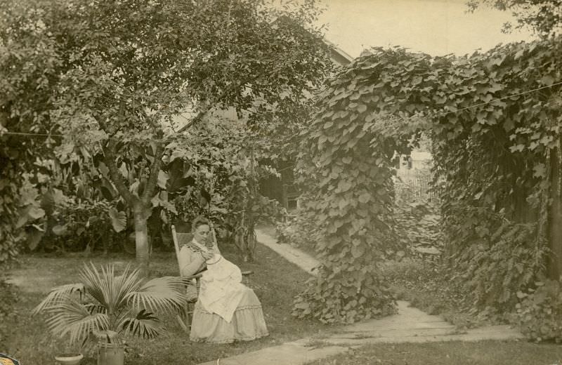 Katherine Horack, sitting in a rocking chair in her garden, creating a drawn work tablecloth for her daughter, Bertha, 1895-1897
