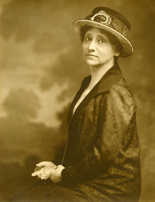 Bertha Shambaugh wears a jacket and skirt with a floral design. Her hat has a matching decorative band, and she holds glasses, circa 1924